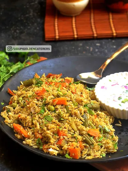 A plate of our flavorful Vegetable Pulao, cooked with long-grain rice, mixed vegetables, and aromatic spices, served with a side of cooling raita.