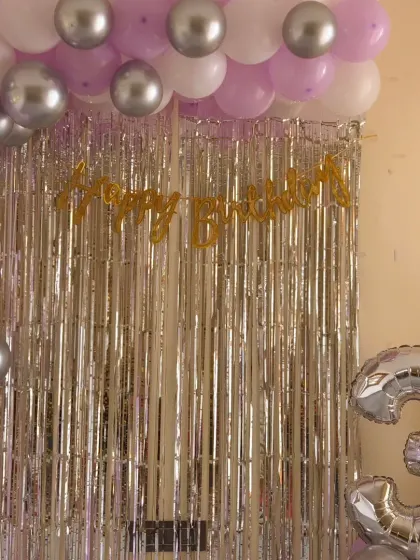 A simple yet elegant home birthday setup. A silver shimmer curtain, a "Happy Birthday" banner, and a balloon arch in purple, white, and silver can transform any room.