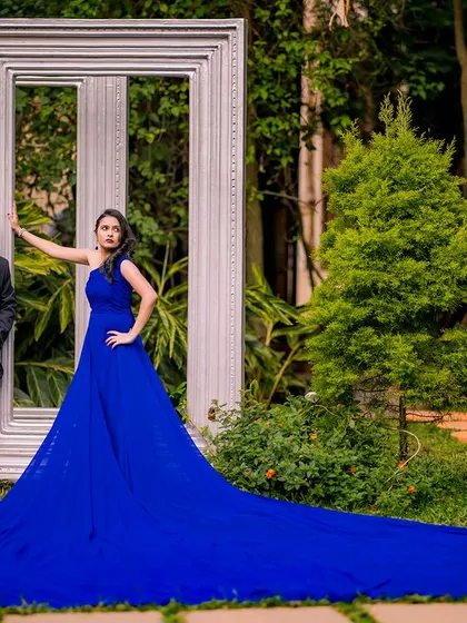 A full-width shot showing the incredible length of the blue trail gown. This is a statement photo that combines fashion, drama, and romance in a beautiful garden setting.