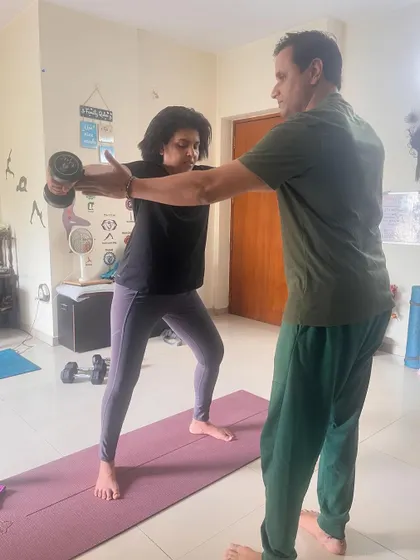 I am providing hands-on assistance to a client to ensure correct form during a dumbbell exercise. This personalized attention is what sets my coaching apart.