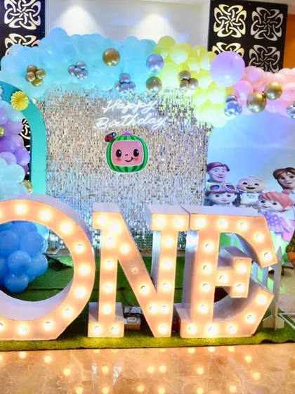 A Cocomelon first birthday party with a silver shimmer wall and pastel-colored balloon arch.
