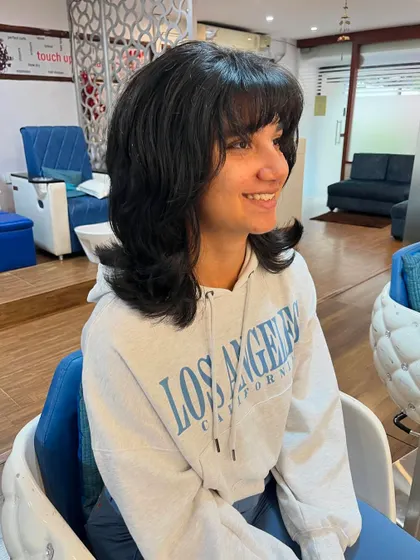 A contemporary shag haircut on Rhea’s thick hair, complete with bangs.