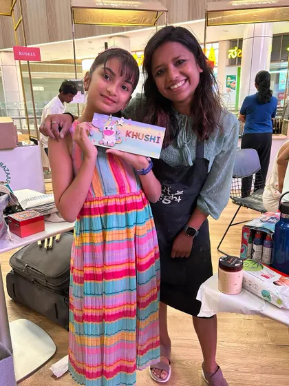 A proud young artist with the colorful nameplate she created at one of our fair stalls.