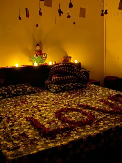 A softly lit romantic room with candles on the headboard and "LOVE" spelled in rose petals on the bed.