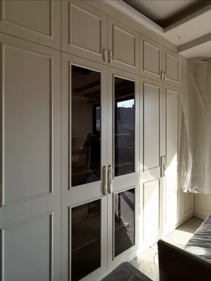 A view of the custom wardrobes during installation, showing the combination of solid and glass-paneled doors that provide both concealed and visible storage.