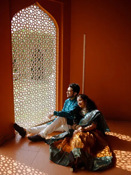 The couple sits by an ornate window, the sunlight casting beautiful geometric patterns on the floor. This quiet, contemplative moment is full of warmth and artistic beauty, perfect for a heritage-themed shoot.