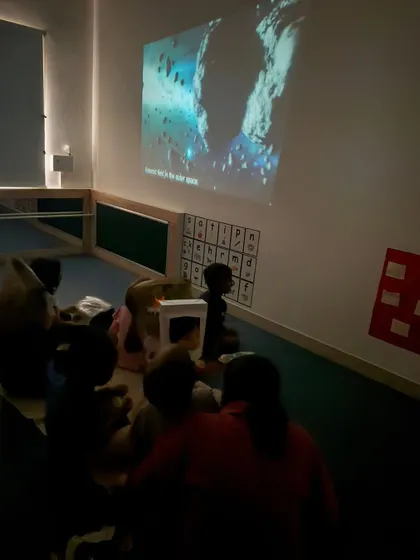 Children sit together and watch a video about asteroids and outer space. Visual media like this helps make complex scientific topics understandable and exciting for young learners.