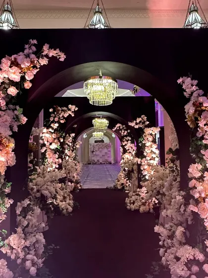 A journey through a tunnel of elegance. This walkway, framed by dark arches and cascading white and pink blossoms, leads guests into a magical reception space.