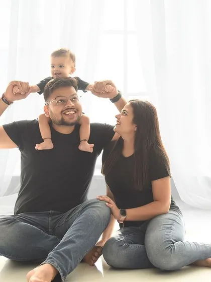 A playful family moment, with dad lifting their little one high. The simple, bright background keeps the focus on their happy interaction.