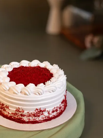 A vibrant Red Velvet bento cake. The deep red cake is a beautiful contrast to the pure white cream cheese frosting, finished with a piped border and a sprinkle of cake crumbs.