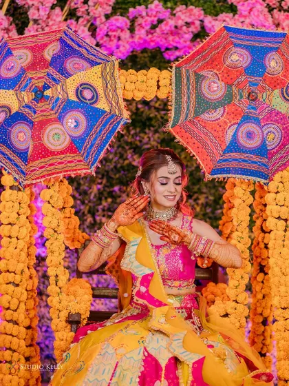 A beautiful shot of the bride at her Mehendi ceremony, seated against a vibrant backdrop of marigolds and colorful umbrellas.