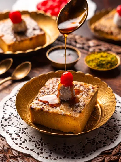 A classic bread pudding dessert from Gallops, with caramel being drizzled on top. The use of brass plates and warm lighting gives it a comforting, traditional feel.