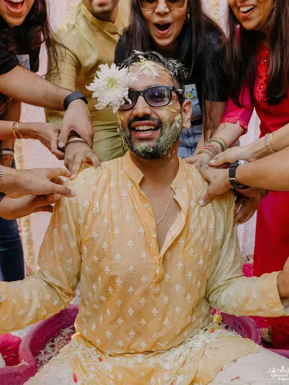 The groom gets playfully smeared with Haldi by his friends, a classic candid moment of fun and laughter.