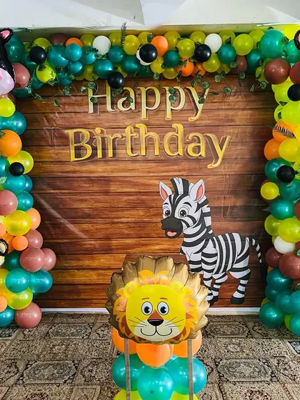 A jungle theme backdrop with a wood-panel look. The balloon arch is filled with animal characters like a monkey, lion, and zebra.