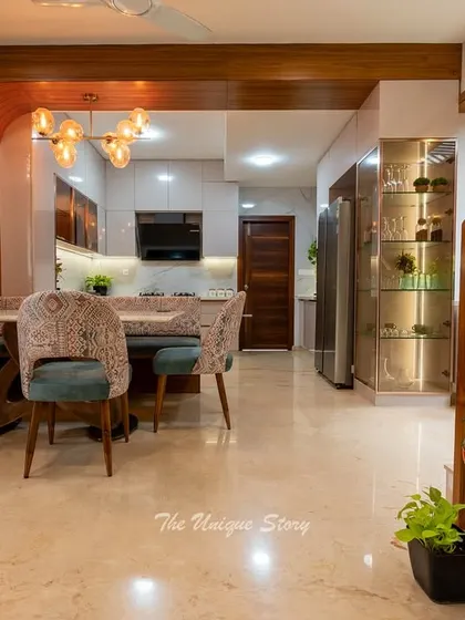 This open kitchen and dining area is a perfect example of modern Indian design. The L-shaped kitchen features sleek cabinets and a marble backsplash, while a decorative wooden archway and partition elegantly frame the space.