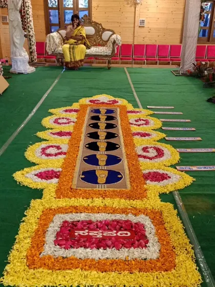 A traditional floral rangoli designed for the Saptapadi ritual, where the couple takes their seven sacred steps. The design is made with colorful flower petals on a green carpet.
