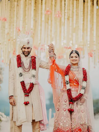 A moment of triumph and togetherness after the Varmala. The couple holds hands, celebrating their union under a breathtaking canopy of flowers.