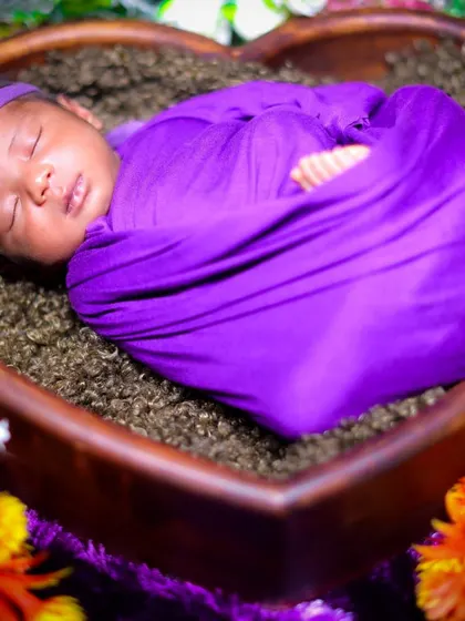 A precious newborn photo of a baby wrapped in a purple swaddle, sleeping peacefully in a heart-shaped wooden bowl.