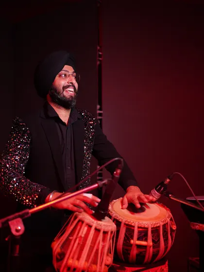 A candid shot of me playing tabla during a live show, with a sequined jacket that adds to the stage presence for evening events.