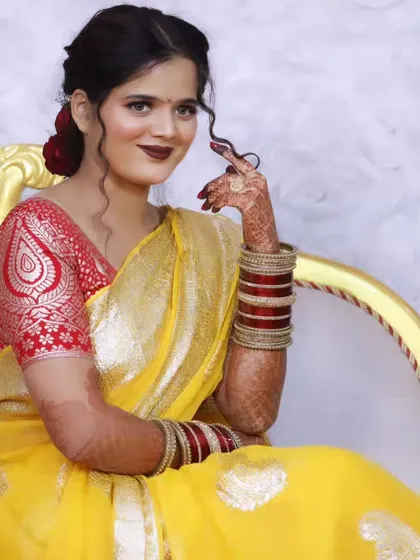 A North Indian bride in a vibrant yellow saree, her look completed with a bold lip and traditional red and white bangles.