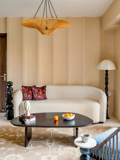 Part of our 'Project Lily,' this living area features a comfortable, modern curved sofa, a sleek dark wood coffee table, and a statement rattan chandelier, creating a warm and inviting atmosphere.