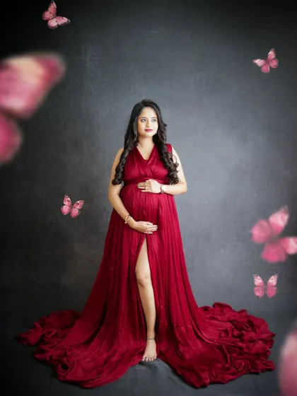 A magical portrait with butterfly effects. The mom-to-be stands in a beautiful red gown, surrounded by fluttering butterflies, creating a whimsical scene.