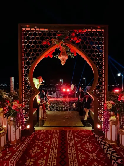 An opulent entrance for a celebration in Doha, glowing under the night sky. The design features intricate latticework, golden lanterns, and a traditional patterned rug. ⭐️