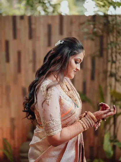 A side profile of the bride, showing the delicate embroidery on her sheer blouse sleeves and her beautiful, flowing hair.