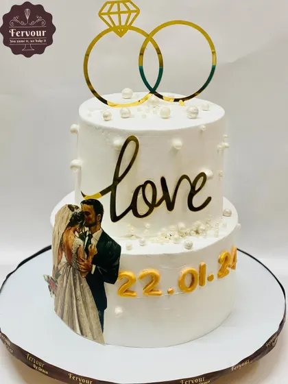 A lovely two-tier wedding anniversary cake featuring the couple's photo and their wedding date. The simple "Love" topper and pearl details make it a sweet and personal way to celebrate.