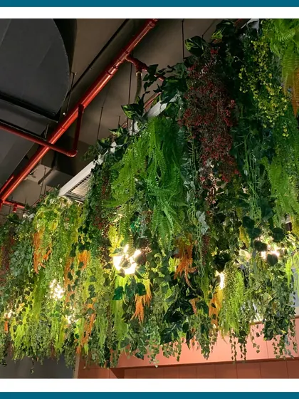 A different angle of a dense artificial hanging installation, with integrated lights peeking through the foliage. This creates a beautiful play of light and shadow, adding depth and a magical quality to the indoor canopy.
