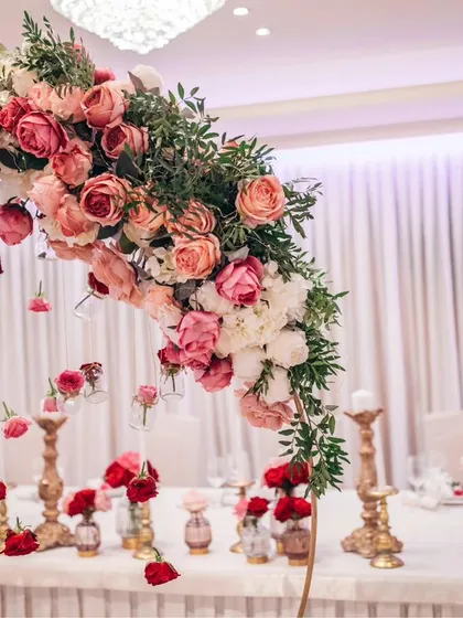 Attention to detail is key. This elegant wedding table setting features a cascading floral centerpiece with pink and red roses, complemented by golden candelabras and individual rose buds in small vases.