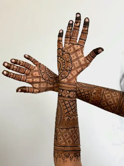 A dynamic pose showing a full-arm bridal mehendi, demonstrating the extensive coverage and detailed patterns.
