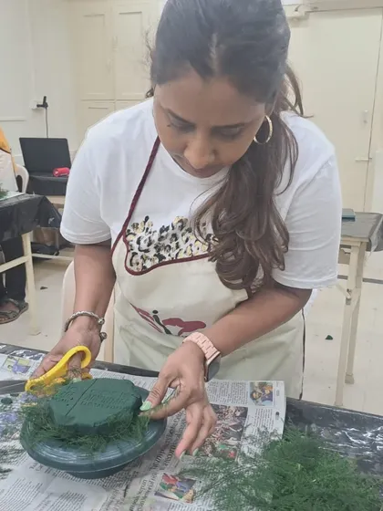 Concentration and precision in action. A student in our advanced course focuses on shaping the floral foam, ensuring a stable and well-proportioned base for her arrangement. This attention to detail is a hallmark of professional floristry.