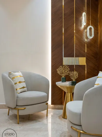 We love creating cozy conversation corners. This setup features two plush grey armchairs with elegant gold-finished legs, set against a backdrop of rich wood paneling and statement pendant lights. It’s a perfect example of a small space designed with luxury in mind.