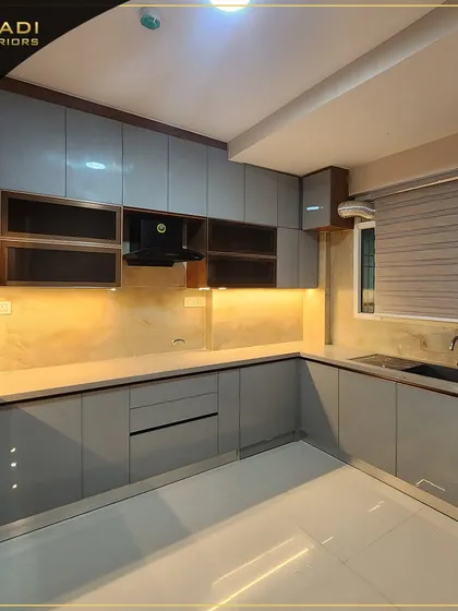 A sleek, modern kitchen in a grey high-gloss finish. The design includes under-cabinet lighting that illuminates the countertop and backsplash, creating a warm and functional workspace.