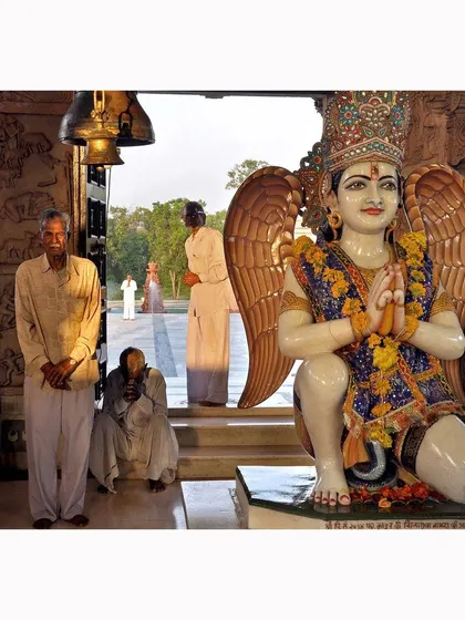 Devotees at the entrance of a temple, with a statue of Garuda in the foreground. The image captures the peaceful expressions of the people and the ornate details of the sacred art.