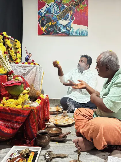 I am participating in the Saraswati Pooja with a senior member of our community. The painting of a sitar player on the wall was a gift from a student.