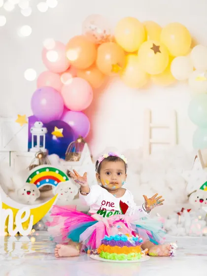 A rainbow-themed cake smash for a colorful first birthday. This setup is complete with a rainbow balloon arch, clouds, and a matching cake.