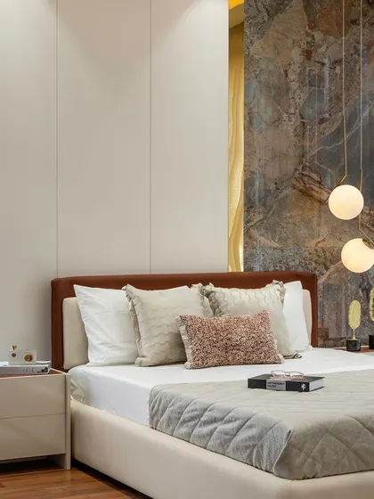This bedroom combines soft textures with a bold feature wall. The bed, with its layers of plush pillows, is set against a dramatic, stone-like wall panel. Spherical pendant lights add a modern, artistic touch to the serene space.