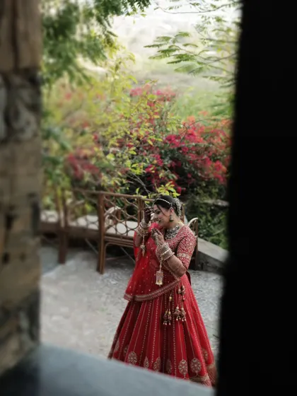 A candid shot of the bride, framed through a window, as she adjusts her veil in a garden setting.
