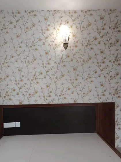 A bedroom accent wall with a delicate cherry blossom wallpaper. The wall-mounted lamp highlights the beautiful pattern.