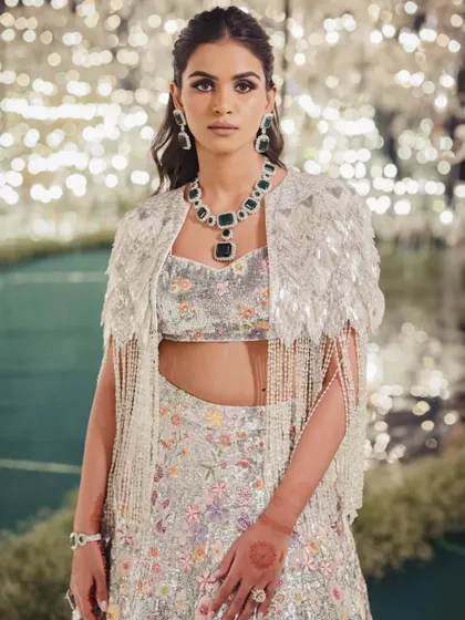 A bride styled in a stunning floral lehenga with a feathered and beaded cape. This look, featured by WeddingSutra, showcases a blend of modern trends and classic elegance.