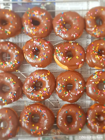 Freshly glazed chocolate donuts with colorful sprinkles, cooling on a rack. These are a very popular item in our kids' party boxes.