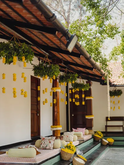 The venue's verandah is transformed into a comfortable and festive seating area with low mattresses, colorful cushions, and hanging marigold decorations.
