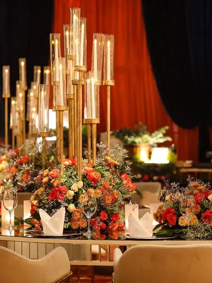 A beautiful tablescape from the Diwali party, featuring a tall candelabra centerpiece surrounded by a wreath of orange and red flowers. The dark blue drapes in the background provide a rich contrast.