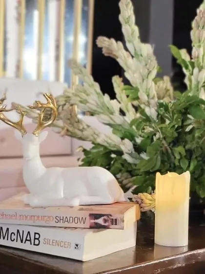 A charming decor detail featuring a white deer figurine, vintage books, and a flameless candle, perfect for adding a personal touch to a welcome table.