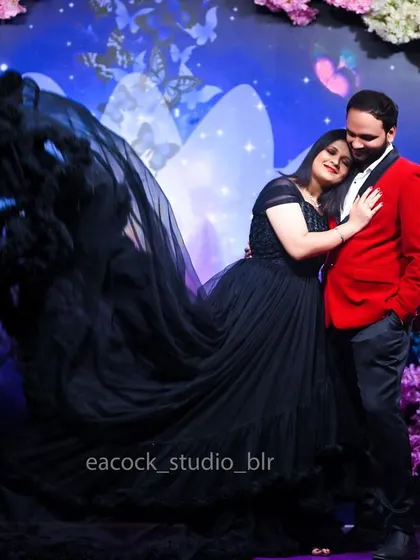 A tender moment from a pre-wedding shoot, with the couple embracing. The woman's black trail gown and the man's red blazer stand out against the colorful studio backdrop.