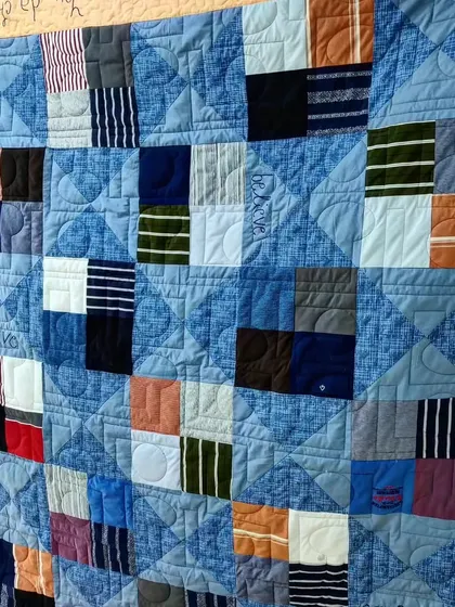 A close-up of a memory quilt made from blue-toned T-shirts, with custom words like "Love" and "Believe" quilted in.