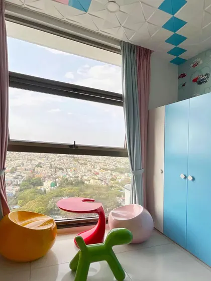 This vibrant kids' room at Sobha Indraprastha is designed for play. Colorful, child-safe furniture and a geometric patterned ceiling create a cheerful atmosphere, with a large window offering expansive city views.