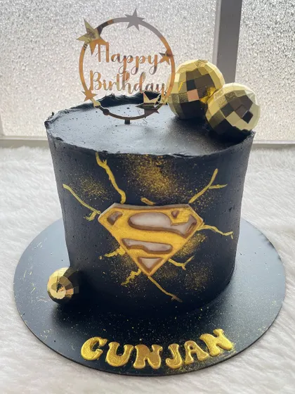 A dark and dramatic Superman cake. The black ganache is airbrushed with gold, and the iconic 'S' logo is front and center, making for a powerful design.